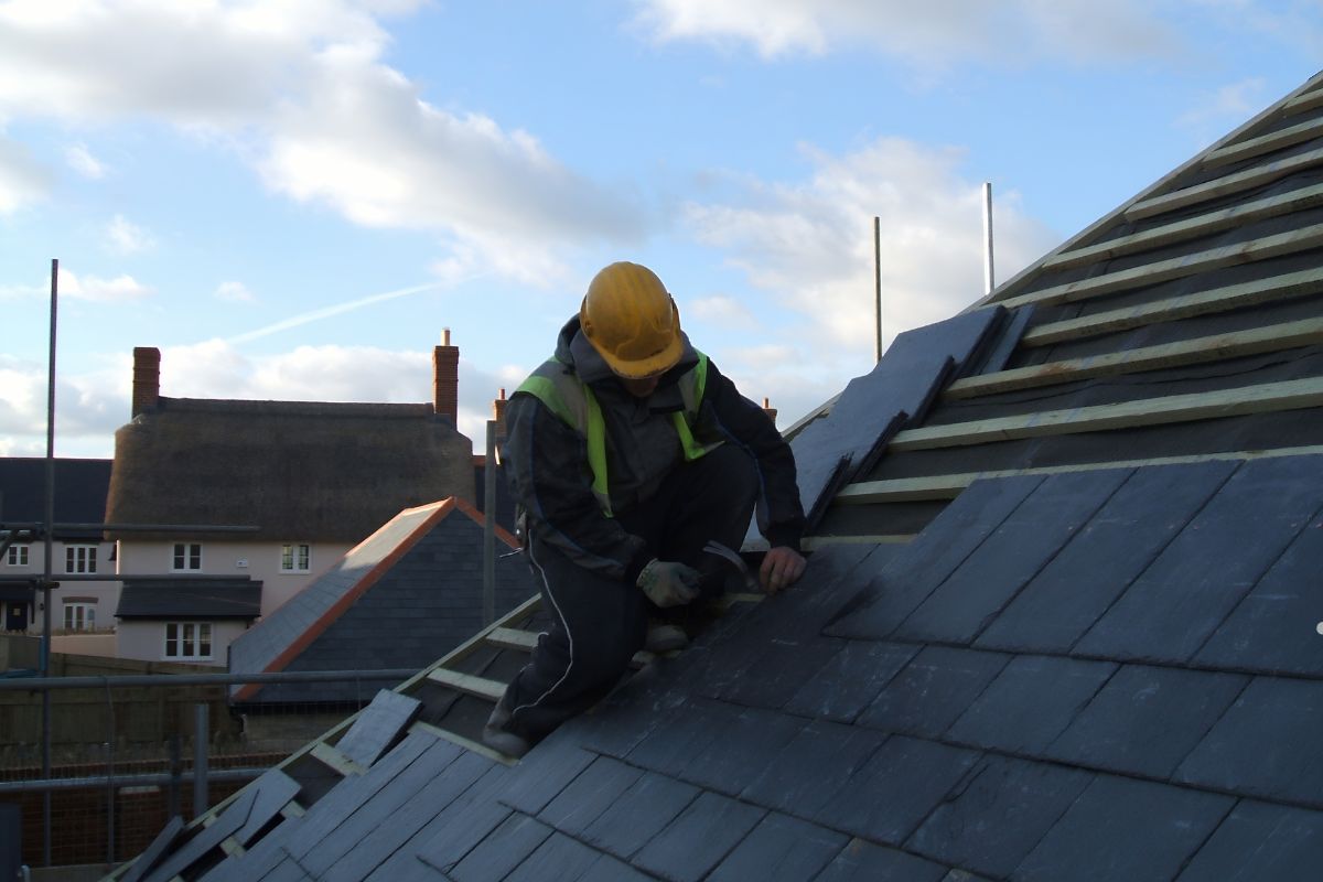 A man using a hammer to work on a roof, focused on his task while standing on the sloped surface.